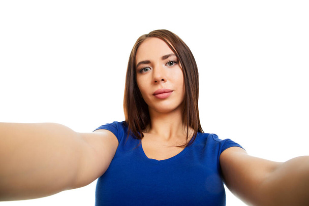 Una bella ragazza prende un selfie, tenendo la fotocamera con entrambe le mani a lato. Isolato su sfondo bianco. - Foto, immagini