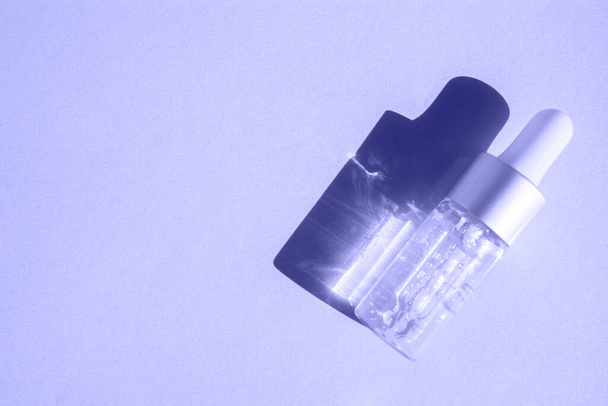 Una botella de cuentagotas de vidrio con loción cosmética sobre un fondo sólido proyecta una sombra. Vista superior, lugar para texto. Producto cosmético. Color de moda del año 2022. - Foto, Imagen