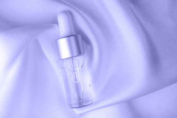 Botella de vidrio con líquido cosmético sobre tela de seda. Vista superior, primer plano. Color de moda del año 2022. - Foto, Imagen