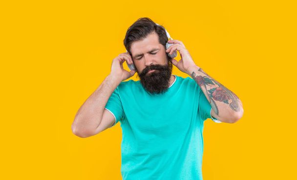sleepy dj guy in music headphones isolated on yellow background. dj guy wearing music headphones in studio. guy listen music in dj headphones. music in headphones of guy dj. - Foto, afbeelding