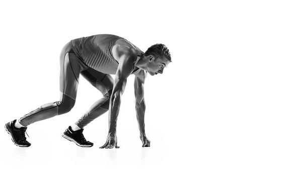 At start line. Black and white portrait of muscular male athlete, runner, jogger in motion isolated on white background. Monochrome. Sport, beauty, power and style. Copy space for ad, text - Foto, imagen