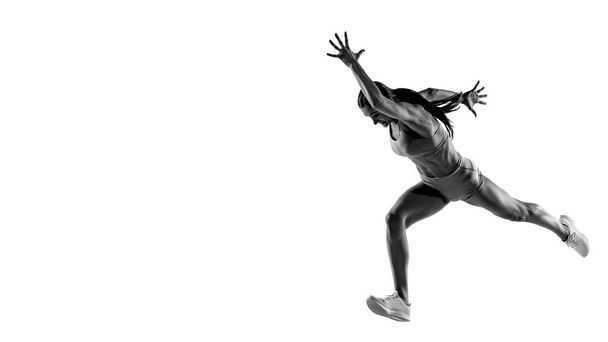Speed and power. Black and white portrait of professional female athlete, runner, jogger in action isolated on white background. Monochrome. Sport, beauty, power and style. Copy space for ad, text - Foto, afbeelding