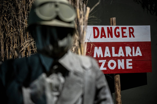 Σημάδι κινδύνου που χρησιμοποιήθηκε κατά τη διάρκεια του Δευτέρου Παγκοσμίου Πολέμου σε περιοχές απολύμανσης της ελονοσίας - Δίπλα σε έναν άνδρα με στολή της εποχής με μάσκα αερίου - Φωτογραφία, εικόνα