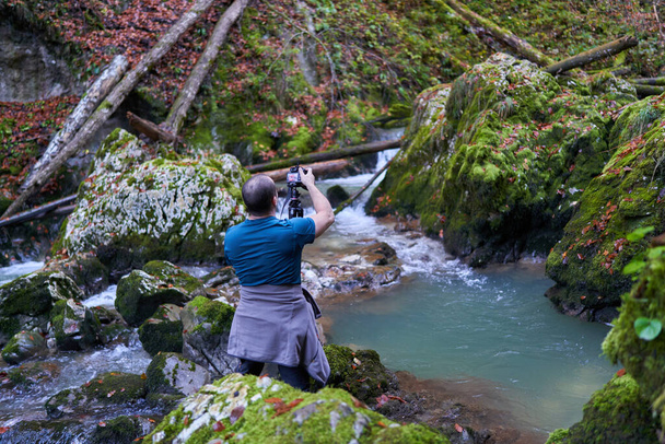 Nature photographer shooting landscapes in a canyon covered in moss and luxuriant vegetation, with a river  - Fotografie, Obrázek