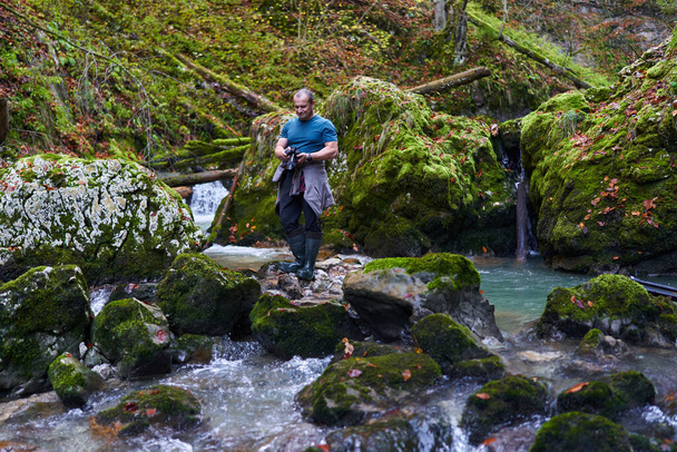 Nature photographer shooting landscapes in a canyon covered in moss and luxuriant vegetation, with a river  - Foto, imagen