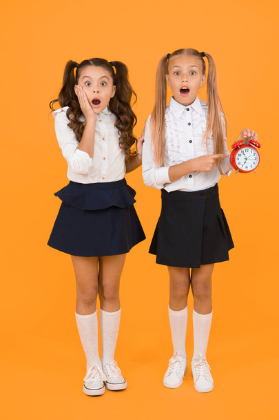 OMG. Got a surprise. Surprised schoolgirls checking time on yellow background. Shocked little children having mouth open with surprise being late. Back to school surprise. Surprise concept. - 写真・画像