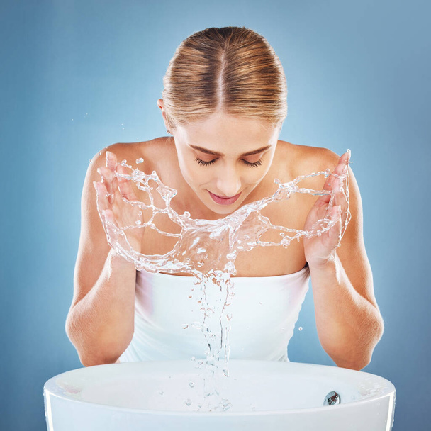 Γυναίκα, νερό ή πλύσιμο προσώπου σε περιποίηση skincare σε μπλε στούντιο φόντο από νεροχύτη ή λεκάνη. Μοντέλα ομορφιάς, υγρό και καθαρισμό προσώπου με νερό για συντήρηση υγιεινής, υγειονομική περίθαλψη ή ευεξία. - Φωτογραφία, εικόνα