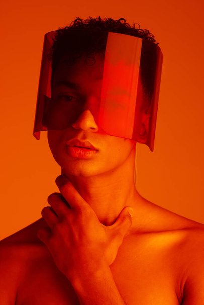Orange, futuristic and man with a neon visor for cyberpunk, creative style and art against a studio background. Digital, fashion and face portrait of a model with a designer product for future. - Foto, afbeelding