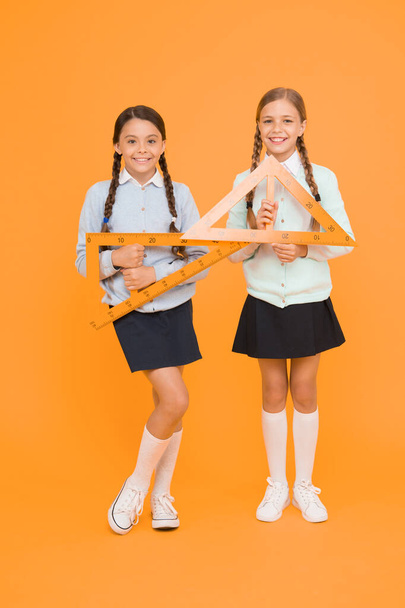 Move from theory to practice. Excellent pupils. Secondary school. Schoolgirls tidy appearance school uniform hold big rulers for geometry school lesson. Kids cute students study math. Knowledge day. - Valokuva, kuva