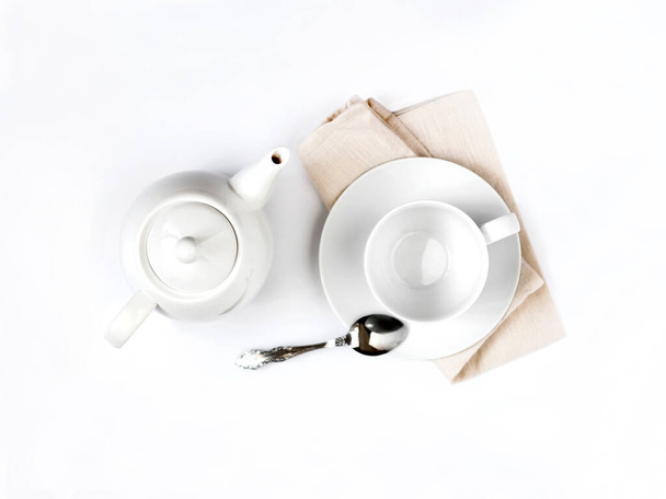 White teapot and empty teacup with spoon on pale beige cloth isolated on white background. Flat lay, top view - Fotó, kép