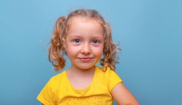 Little girl in a yellow T-shirt on a blue background. - Фото, изображение