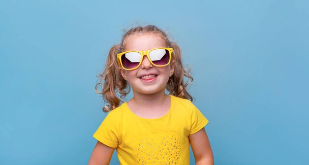 Little girl in yellow sunglasses on a blue background. - Foto, afbeelding