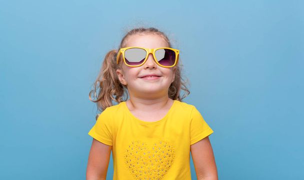 Sárga napszemüveges kislány kék háttérrel. - Fotó, kép