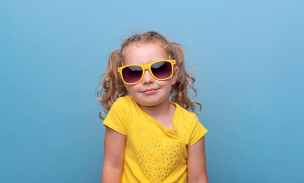 Little girl in yellow sunglasses on a blue background. - Photo, Image