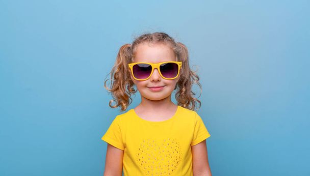 Petite fille en lunettes de soleil jaunes sur fond bleu. - Photo, image