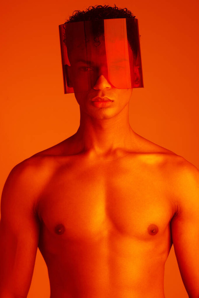 Body, glasses and red with a man model in studio on a color background for trendy or edgy fashion. Portrait, topless and style with a handsome young male wearing eyewear under bright lighting. - Φωτογραφία, εικόνα