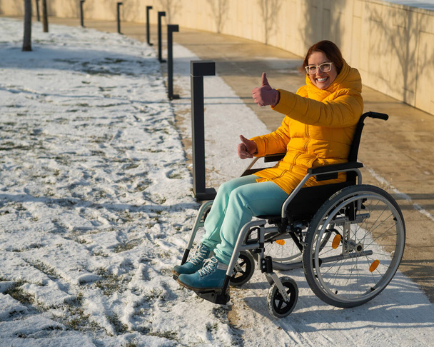 Caucasian woman showing thumb up in wheelchair in winter park - Foto, afbeelding
