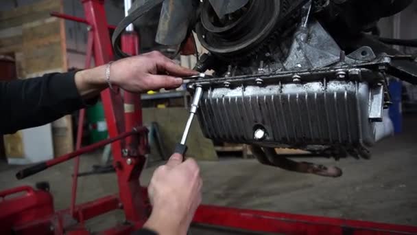 een monteur demonteert een oude smerige automotor op een rode lift voor reparatie en afstelling - Video