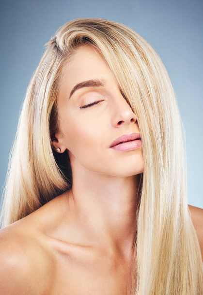 Face, beauty and hair care of woman with eyes closed isolated on blue background in studio. Aesthetic, luxury makeup or skincare of female model with long, blonde or healthy hair after hair treatment. - 写真・画像
