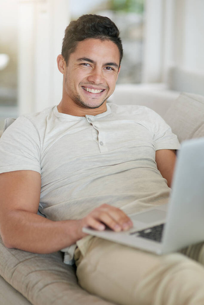 This is how we millennials relax. Portrait of a relaxed young man using a laptop on the sofa at home - Foto, Imagem