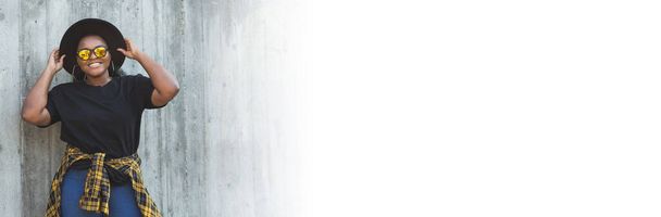 Баннер красивый афроамериканский хипстер тысячелетия девушка смотрит на камеру улыбается носит солнцезащитные очки и шляпу, стоя напротив стены, копировать пространство и пустое пространство для текста - Фото, изображение