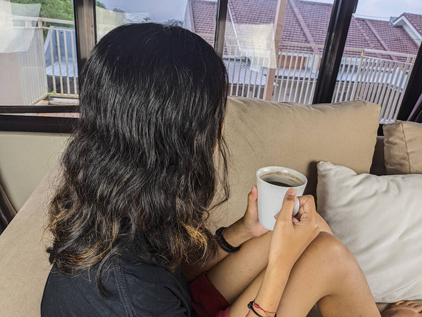 Una joven bebió un vaso de café en el sofá mientras se relajaba. Vacaciones de Navidad y Año Nuevo - Foto, Imagen