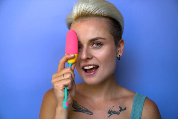 Portrait of short haired woman close one eyes behind colourful vaginal egg and looking playfully to the camera. Sex toys and orgasm concept - Zdjęcie, obraz