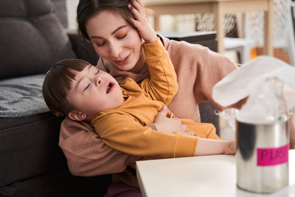 Caucasian woman embracing her son while sitting at the table at home. Family relationships and happy childhood concept - 写真・画像