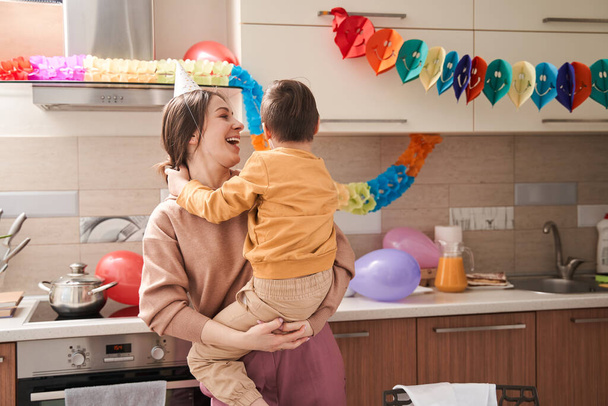Waist up portrait view of the overjoyed woman holding at the hands her male child with genetic disorder while having fun at the kitchen - Photo, Image