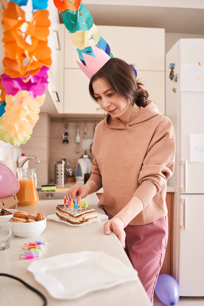 Vertikální pohled na pozornou ženu zdobí narozeninový dort svíčkami, zatímco tráví čas v kuchyni. Koncept oslav - Fotografie, Obrázek