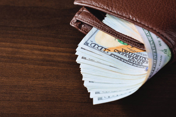 Detailní záběr hnědé kožené peněženky se stodolarovými bankovkami. Rozumím. Zobrazení vysokého úhlu. - Fotografie, Obrázek