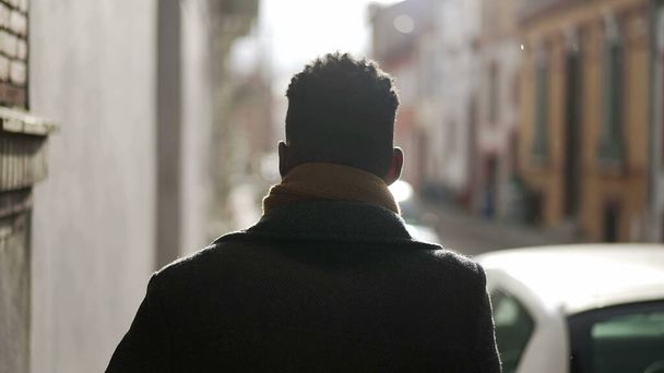 Back of elegant black man walking in city sidewalk during winter season removing scarf - Foto, imagen