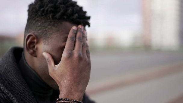 Anxious young black man suffering emotional pain sitting on sidewalk in street - Photo, Image