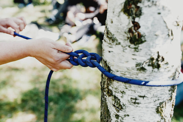 Frauenhände ziehen ein starkes blaues Seil, das an eine Birke gebunden ist. Professionelle Seilbahn- oder Seilbahninstallation. Zeit für Spaß und Entspannung. Familienwochenenden Aktivität zusammen. Hochwertiges Foto - Foto, Bild