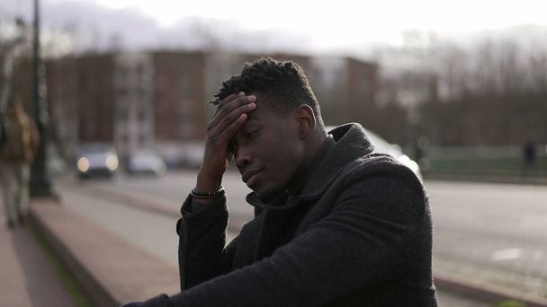 Anxious young black man suffering emotional pain sitting on sidewalk in street - Foto, imagen