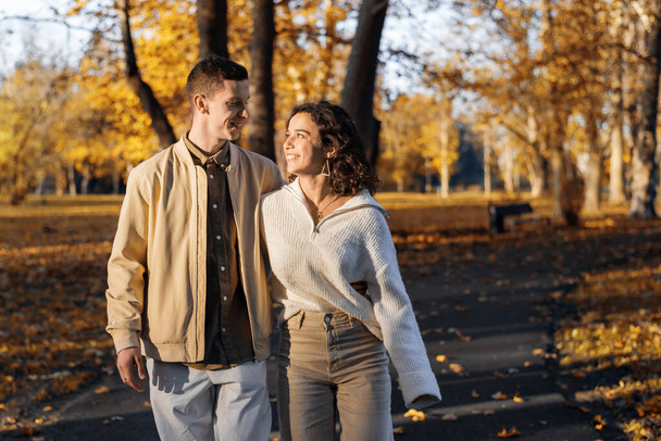 Sonbahar parkında romantik bir çift. Yol boyunca yürüyoruz, birbirimize bakıyoruz. Sonbahar atmosferi, sarı ağaçlar ve yapraklar - Fotoğraf, Görsel