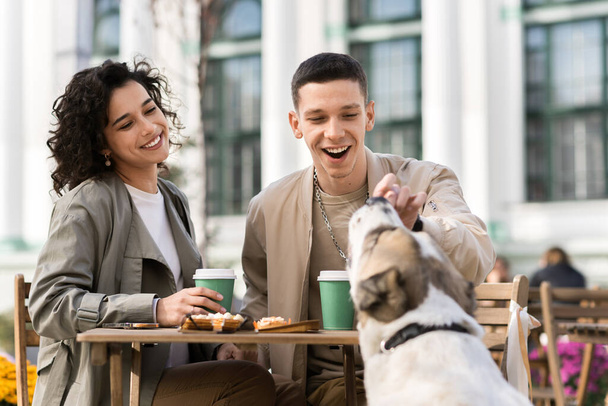 Ein glückliches Paar im Freien in der Nähe eines Cafés. Lächeln, Kaffee auf dem Tisch, Hund. Herbststimmung - Foto, Bild