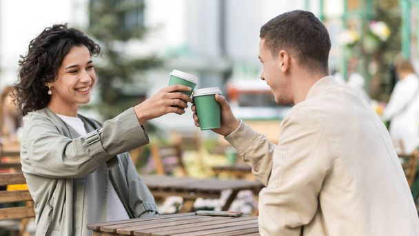 Una pareja feliz al aire libre cerca de un café. Mirándonos, sonriendo, bebiendo café. Ambiente otoñal - Foto, imagen