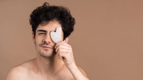 A young caucasian man with stubble beard is posing with Gua Sha - Photo, Image
