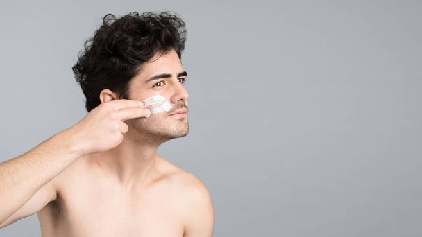 Un giovane uomo caucasico con la barba stoppa sta facendo una maschera facciale - Foto, immagini