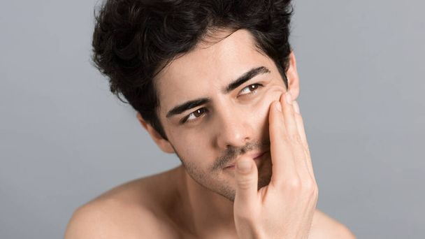 Egy fiatal fehér férfi borostás szakállal hidratálja az arcát és a bőrét kozmetikai olajjal, miközben arcmasszázst végez. - Fotó, kép