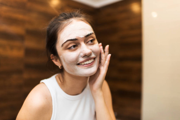 Eine junge kaukasische lächelnde Frau bastelt eine Gesichtsmaske - Foto, Bild