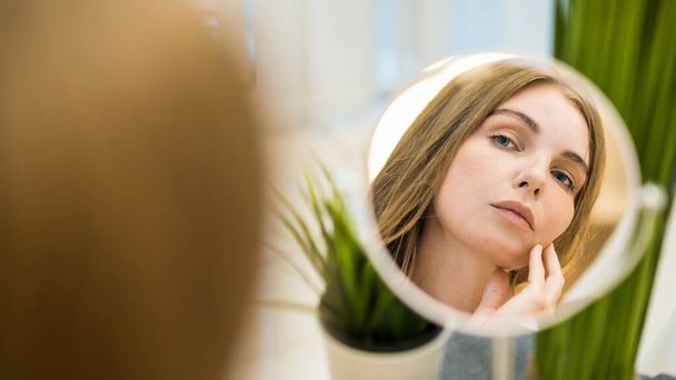 Μια νεαρή λευκή γυναίκα κοιτιέται στον καθρέφτη και ποζάρει - Φωτογραφία, εικόνα