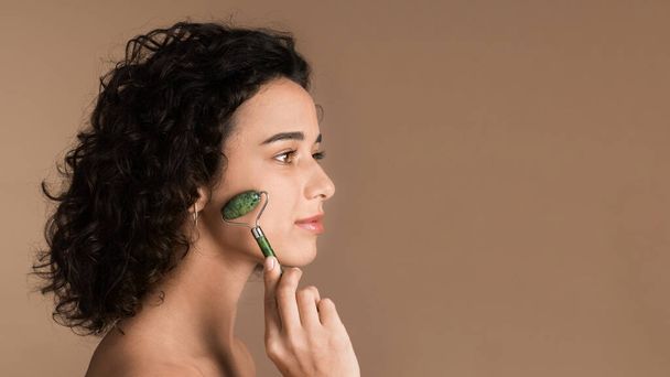 Uma jovem caucasiana está fazendo uma massagem facial usando um rolo - Foto, Imagem