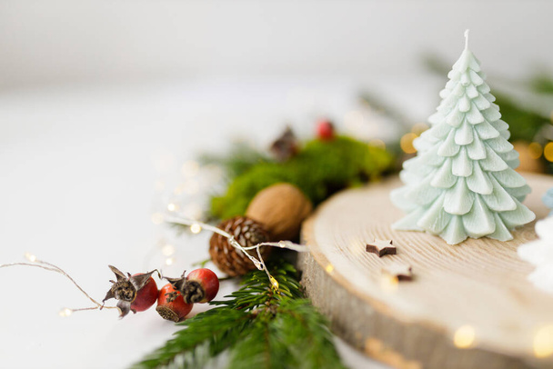 Novoroční dekorativní ručně vyrobená svíčka z přírodního sójového vosku v podobě vánočního stromku na dřevěném stojanu zdobeném větvemi vánočního stromku. Rozumím. Kvalitní fotografie - Fotografie, Obrázek