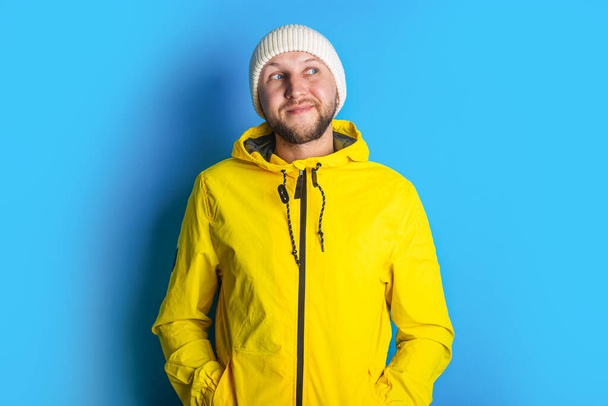 Задумчивый молодой человек в желтой куртке смотрит в сторону на голубом фоне. - Фото, изображение