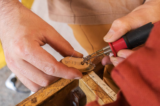 primo piano in vista orizzontale delle mani di un artigiano utilizzando una penna pirografica per incidere il nome LORENA su un portachiavi in legno - Foto, immagini
