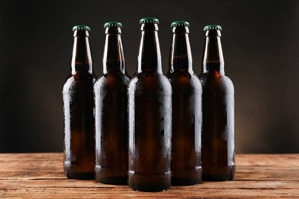 Many bottles of beer on wooden table against dark background - Фото, изображение