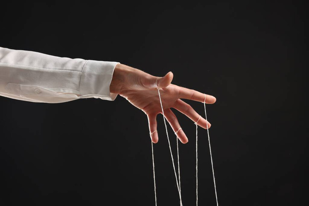 Woman pulling strings of puppet on black background, closeup - Foto, Bild