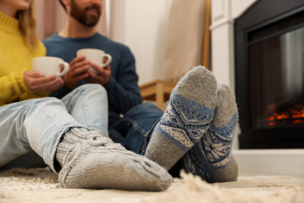 Lovely couple with hot drinks spending time together near fireplace at home, closeup - Photo, image